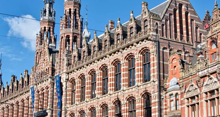 Gedetailleerde gevel van Amsterdam's Magna Plaza met sierlijke bakstenen torens tegen blauwe lucht