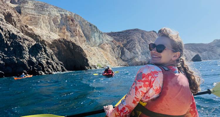 Des kayakistes pagaient dans les eaux bleu profond le long de falaises volcaniques escarpées sous un soleil éclatant.