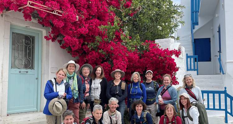 Un grand groupe de femmes sourit devant des bougainvilliers éclatants et une architecture insulaire blanche.