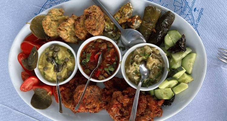 Un plateau de mezzés grecs assortis comprenant des sauces, des légumes et des bouchées frites sur une table blanche.