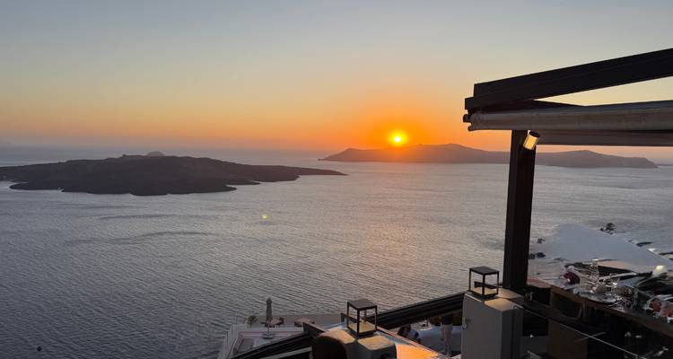 Un coucher de soleil éclatant s'enfonce derrière des îles volcaniques vu depuis une terrasse au sommet d'une falaise.