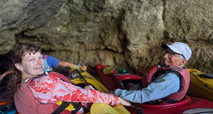 Des kayakeurs se détendent à l'intérieur d'une grotte marine rocheuse en souriant à la caméra.