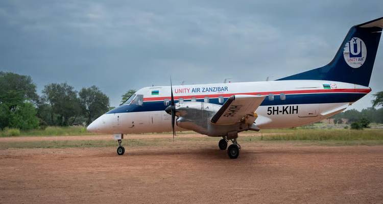 Small Unity Air Zanzibar aircraft on a dirt airstrip under cloudy skies.