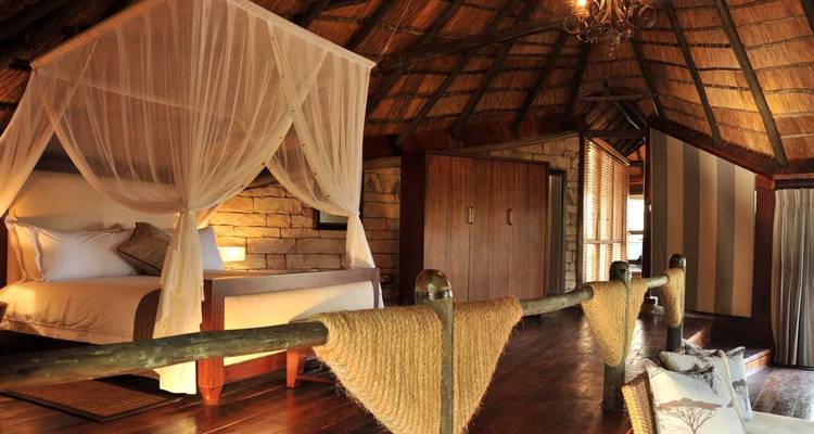 Rustic-luxury safari lodge room with thatched roof, canopy bed and wooden floors.