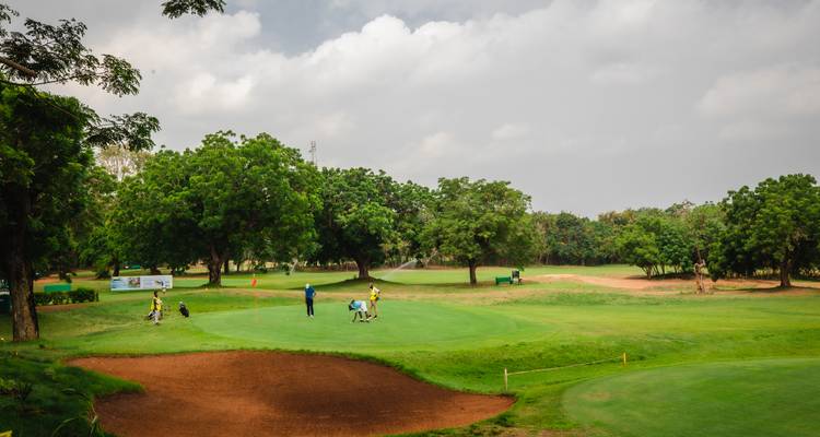 Groene fairway met een kleine groep golfers die putten op een schilderachtige door bomen omzoomde baan.