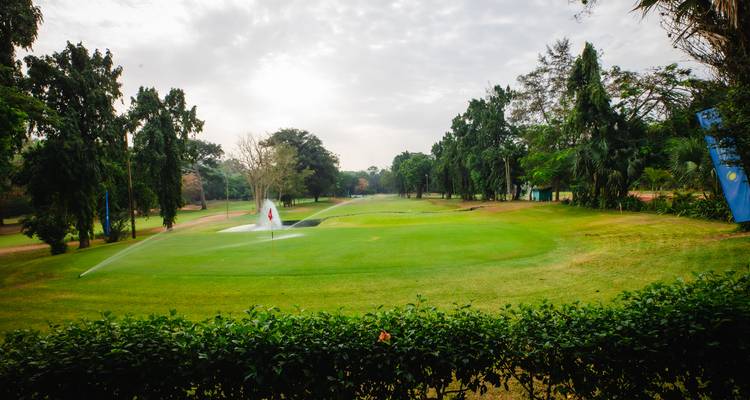 Wijds zicht op weelderig golfgroen met sproeifontein en omringende bossen.