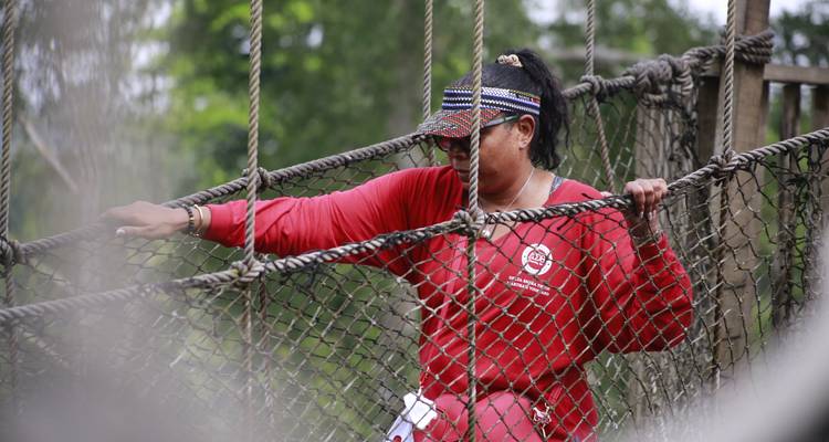 Vrouw steekt voorzichtig een hangende touwbrug over hoog boven het groene regenwoud.