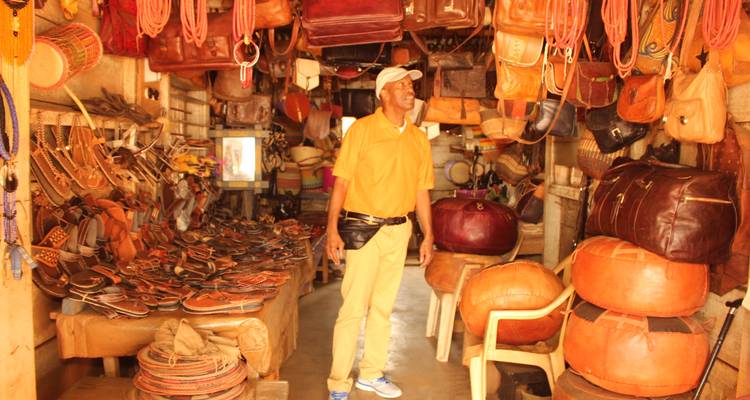 Taller de artesano del cuero repleto de bolsos, sandalias y tambores hechos a mano con el propietario adentro.