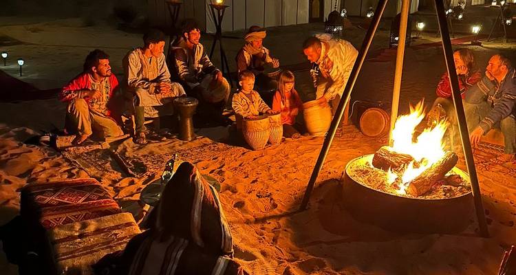 Les voyageurs se rassemblent autour d'un feu de camp éclatant sur le sable du désert, partageant de la musique la nuit.