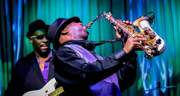 Saxophoniste de jazz énergique en chapeau se produisant sur scène avec un bassiste sous des éclairages colorés