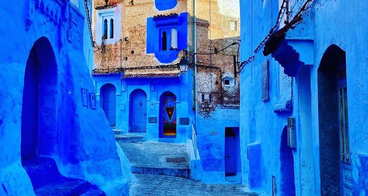 Ruelle étroite de Chefchaouen avec des bâtiments bleus intenses et des portes décoratives.