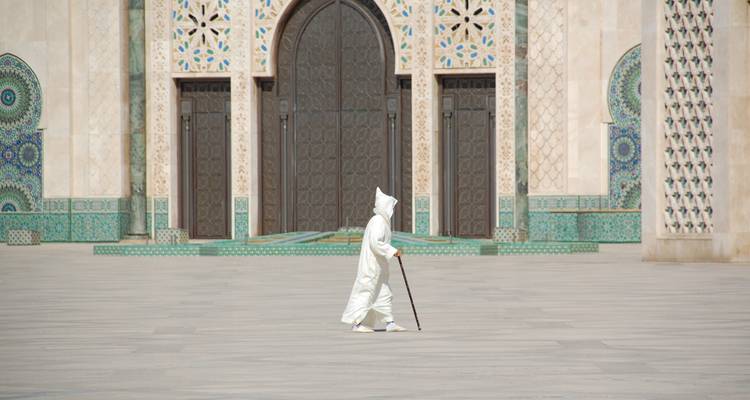 Gestalt in weißer Djellaba, die über den weiten gefliesten Innenhof der Hassan-II-Moschee wandelt.