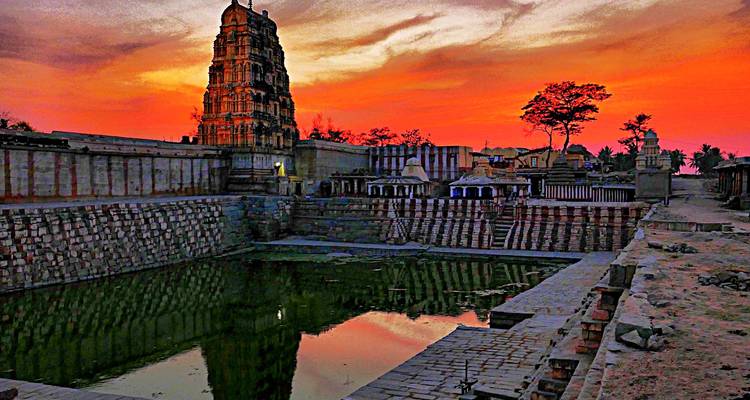Tour de temple ancien reflétée dans un bassin à degrés sous un coucher de soleil orange ardent à Hampi