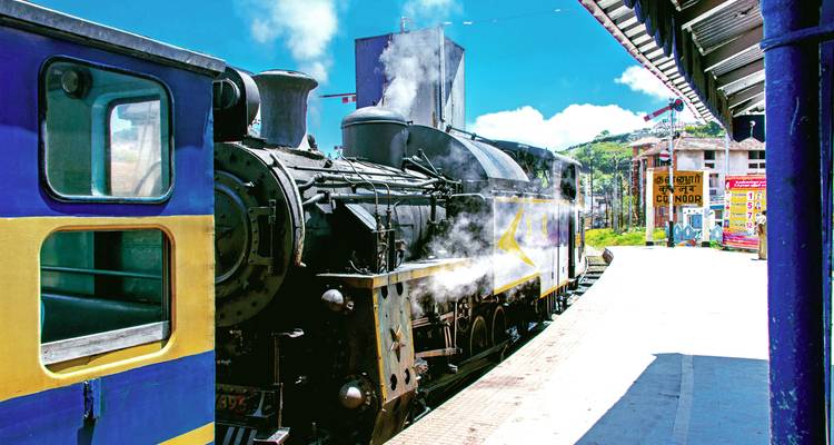 Locomotive à vapeur vintage crachant de la fumée blanche sur un quai de gare de montagne lumineux