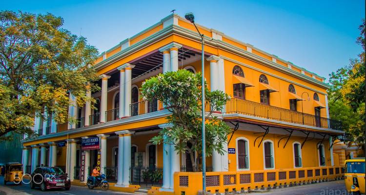 Manoir colonial français jaune avec de hautes colonnes blanches et des arbres tropicaux à Pondichéry