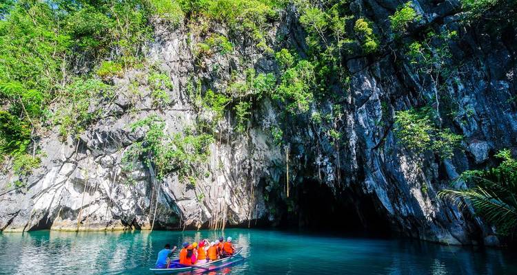 Petite embarcation de visiteurs casqués pénètre dans l'entrée de la grotte calcaire tapissée de jungle au-dessus de l'eau turquoise