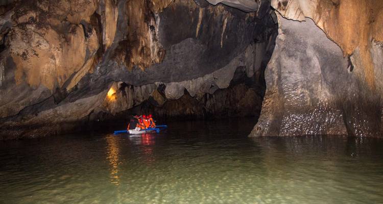 Petit bateau à aubes avec des touristes casqués dérive à l'intérieur d'une vaste grotte calcaire sombre