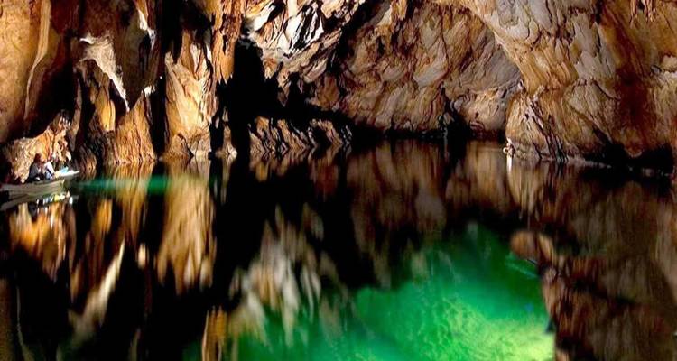 Rivière souterraine illuminée reflète une lumière émeraude sur les parois sculptées de la grotte