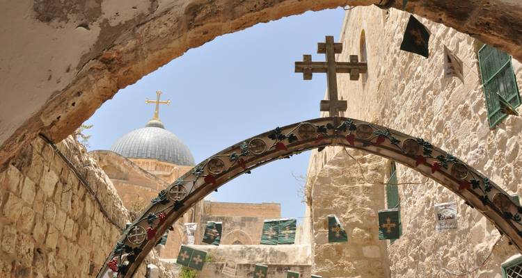 Arcade en pierre avec des croix décoratives encadrant les dômes gris de l'Église du Saint-Sépulcre à Jérusalem