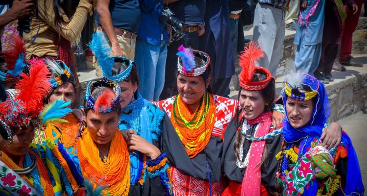 Bunt gekleidete Kalash-Frauen mit gefiederten Kopfschmuck lächeln zusammen während eines traditionellen Festivals.