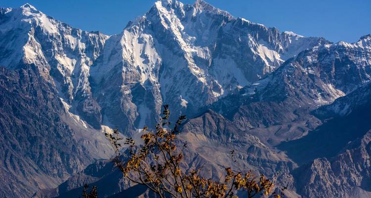 Zerklüftete, schneebedeckte Gipfel ragen majestätisch über kahle untere Hänge unter einem klaren blauen Himmel in Nordpakistan empor.