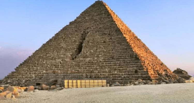 Una pirámide antigua con una grieta diagonal visible está bañada en la cálida luz del atardecer en la llanura del desierto.