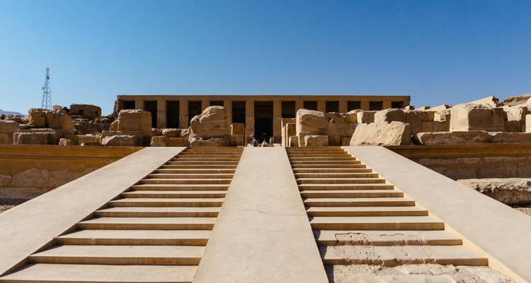 Amplios escalones de arenisca ascienden hacia las ruinas de un antiguo templo mortuorio egipcio bajo un cielo azul despejado.
