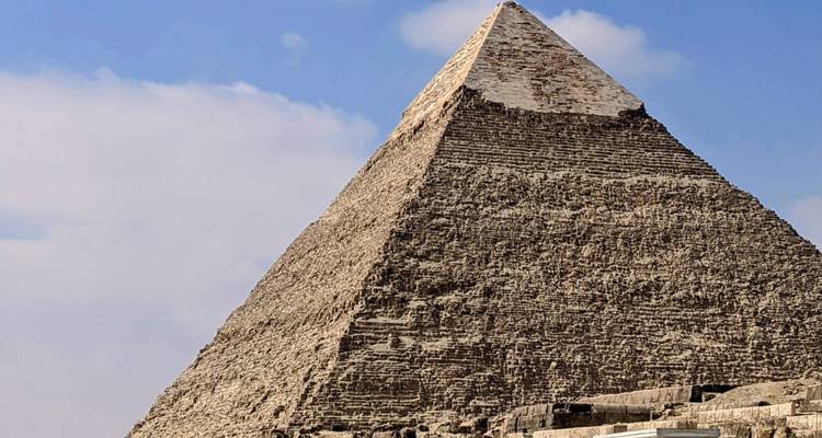 Vista cercana de la Gran Pirámide de Giza con cielo azul y nubes dispersas.