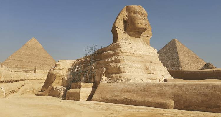 La Gran Esfinge de Giza con dos pirámides al fondo bajo un cielo despejado.