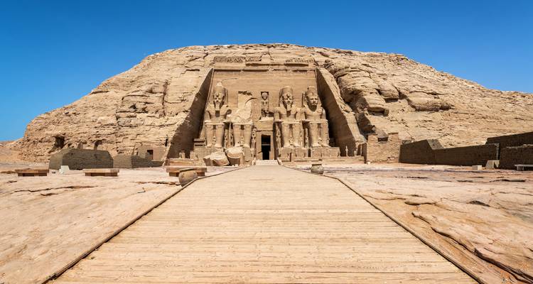 Larga pasarela de madera que conduce a la gran fachada del Templo de Abu Simbel tallado en un acantilado rocoso.