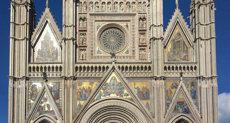 Façade très détaillée d'une cathédrale gothique ornée de mosaïques, de sculptures et d'une rosace sur un ciel bleu profond.