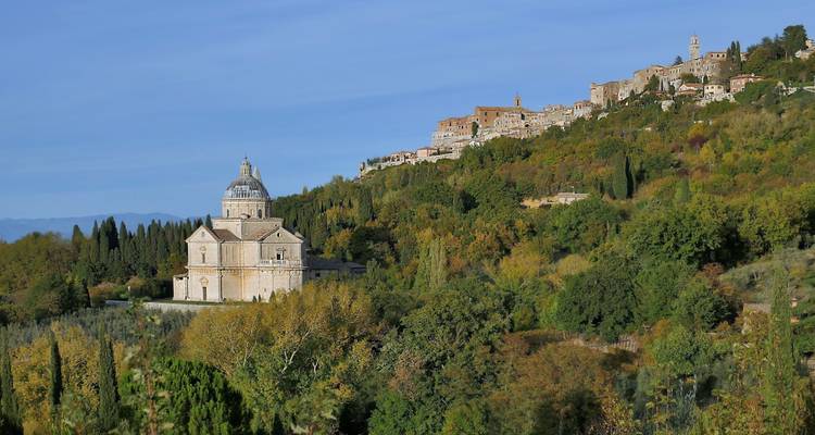 Ville médiévale au sommet d'une colline surplombant une vallée luxuriante avec un sanctuaire à dôme entouré de feuillage d'automne.