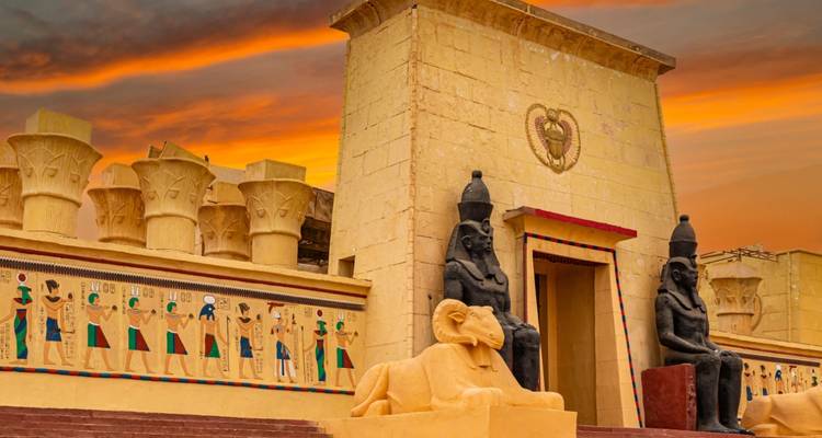 Fachada de templo egipcio estilo escenario de cine con friso de jeroglíficos coloridos bajo un dramático cielo al atardecer.
