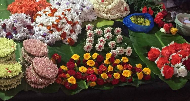 Colorful flower garlands and loose blossoms are artfully displayed on large banana leaves at a market stall.