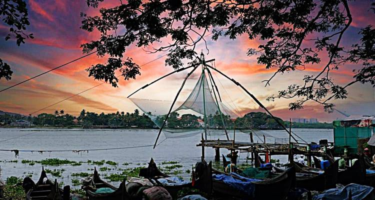 Traditional Chinese fishing nets silhouette against a vibrant sunset sky over the water in Kochi.