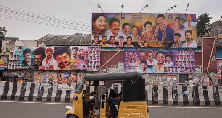 A yellow auto-rickshaw zips past a wall plastered with colourful Tamil film posters.
