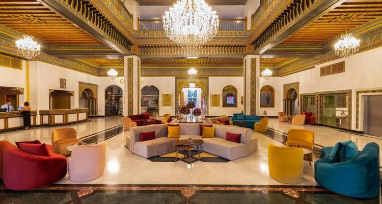 Opulent hotel lobby with colorful seating, ornate Moroccan decor and grand chandeliers.