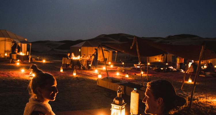 Couple enjoying a candlelit evening at a desert camp with lanterns glowing beneath a starry sky.