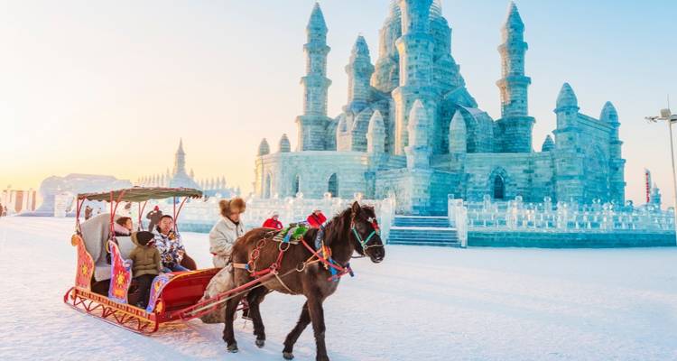 Horse-drawn sleigh carries visitors past an elaborate ice castle at sunrise