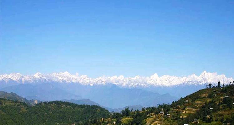 Clear blue sky over a long line of snowy Himalayan peaks above rolling hills.