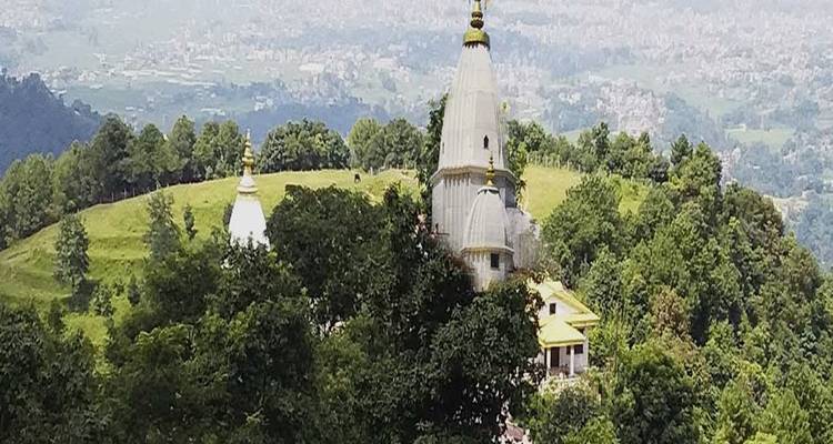 Small white temple spire rises above a verdant hilltop forest with city far below.