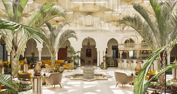 Elegant courtyard lounge with central fountain, arches and tall palm fronds in a luxury Moroccan hotel.
