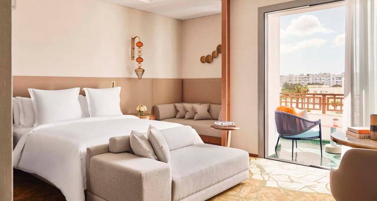 Bright contemporary hotel room with balcony overlooking a city and a small plunge pool.