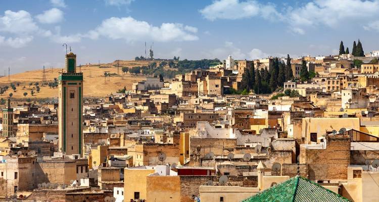Panoramic skyline of Fes with minarets and golden hillside in the distance under blue skies.