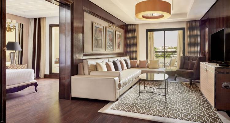 Elegant, well-lit hotel suite with cream sofa, decorative art, and balcony overlooking greenery.