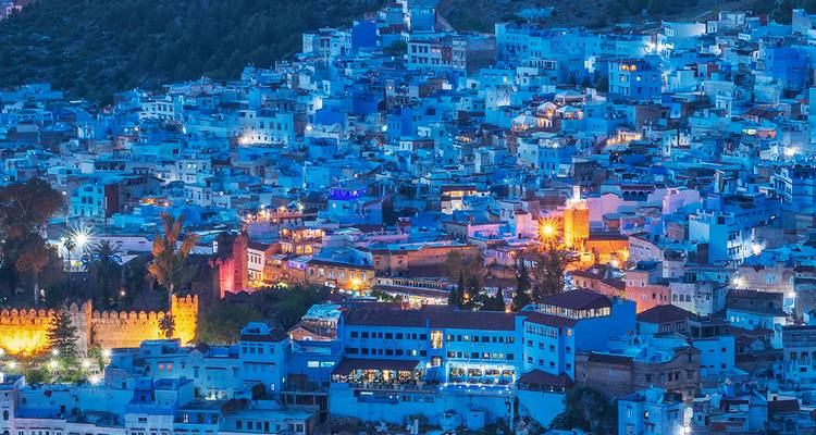 Chefchaouen’s blue houses shimmering with evening lights across a hillside at dusk.