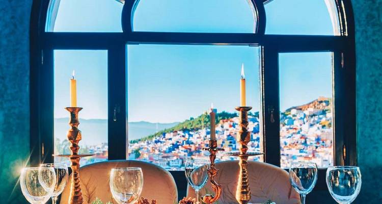 Candlelit dining table in front of an arched window framing Chefchaouen’s blue hillside.