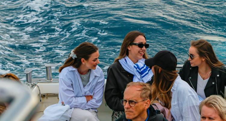 Grupo de viajeros charlando en una lancha rápida con agua azul agitada detrás de ellos cerca de Capri.
