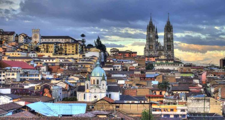 Vista panorámica del horizonte de Quito con techos coloridos y las torres gemelas de la Basílica del Voto Nacional bajo la luz del atardecer.
