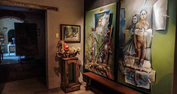 Interior débilmente iluminado de una galería de arte que exhibe pinturas y esculturas modernas.